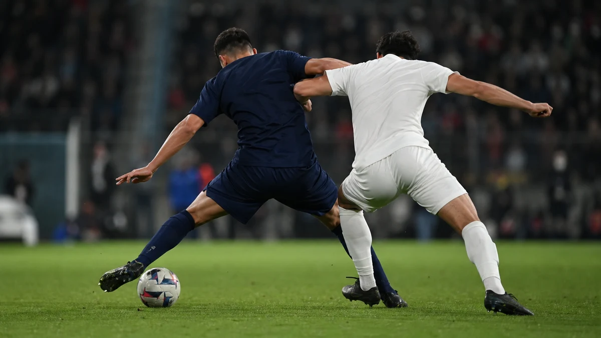 Två spelare i tät kamp om bollen på mittplan under en fransk kvällsmatch